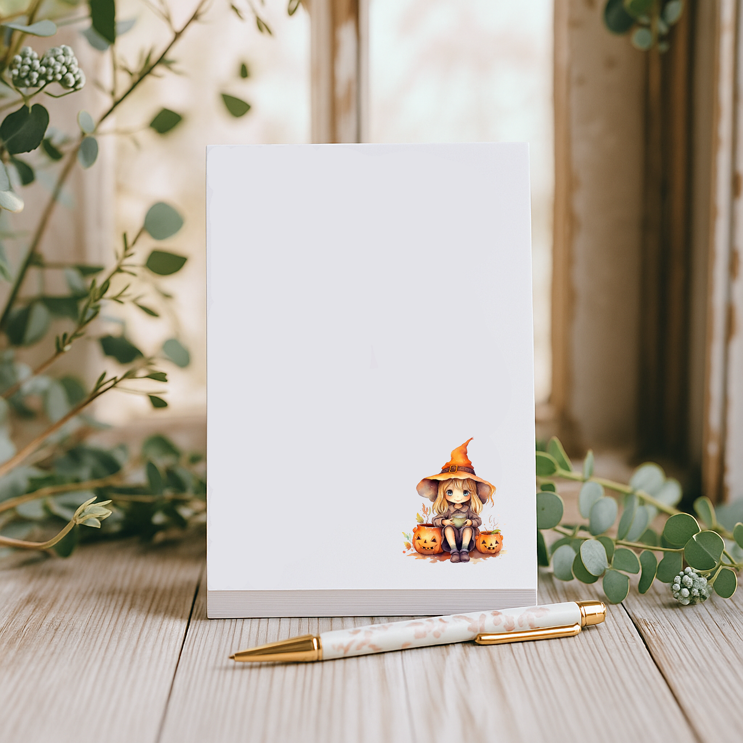 Notebook with a Halloween-themed illustration on a wooden surface with greenery