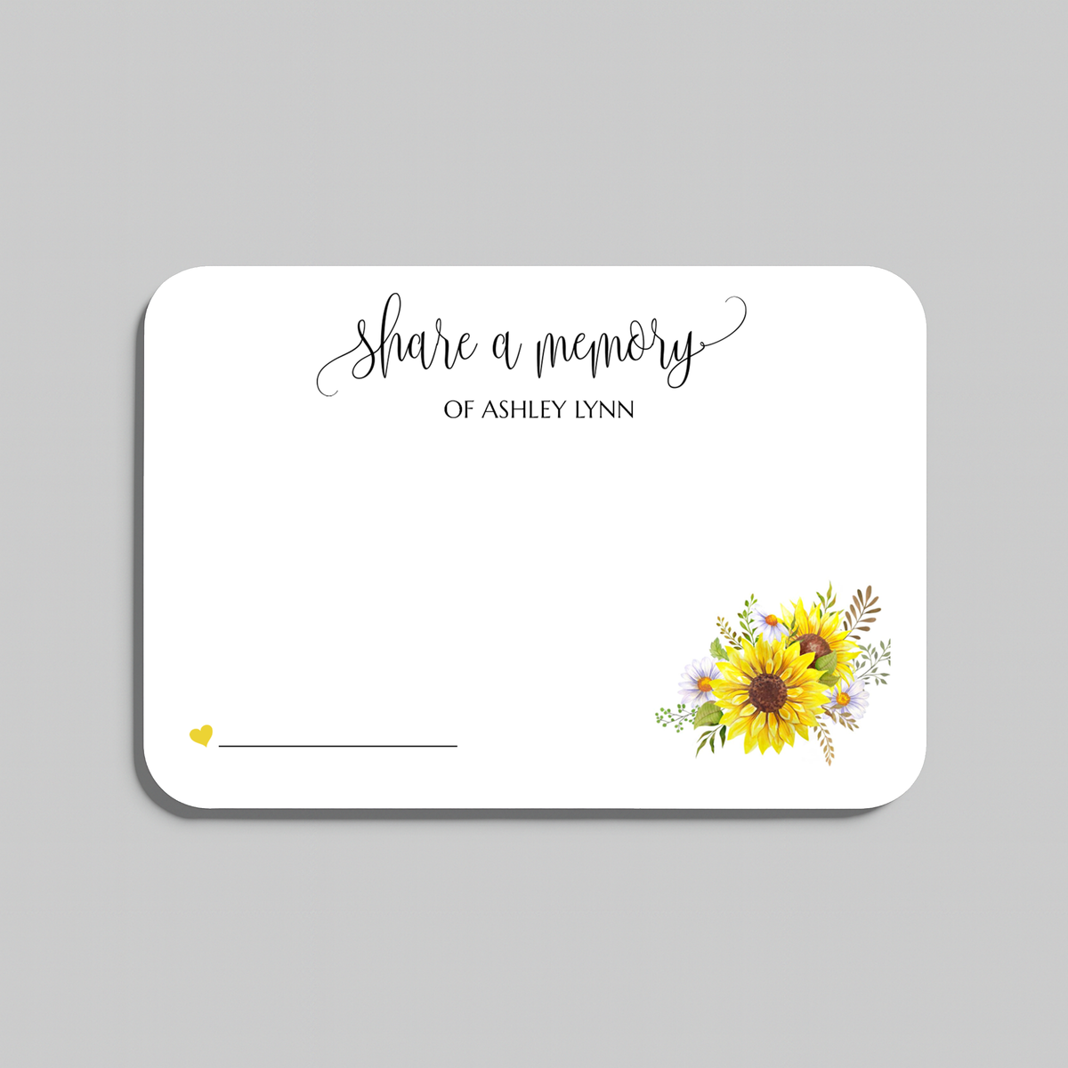 A white memorial keepsake card with rounded corners, featuring the script text 'share a memory' at the top, a small yellow heart and line in the lower left, and a watercolor sunflower and floral arrangement in the lower right. The card is shown on a neutral gray background.
