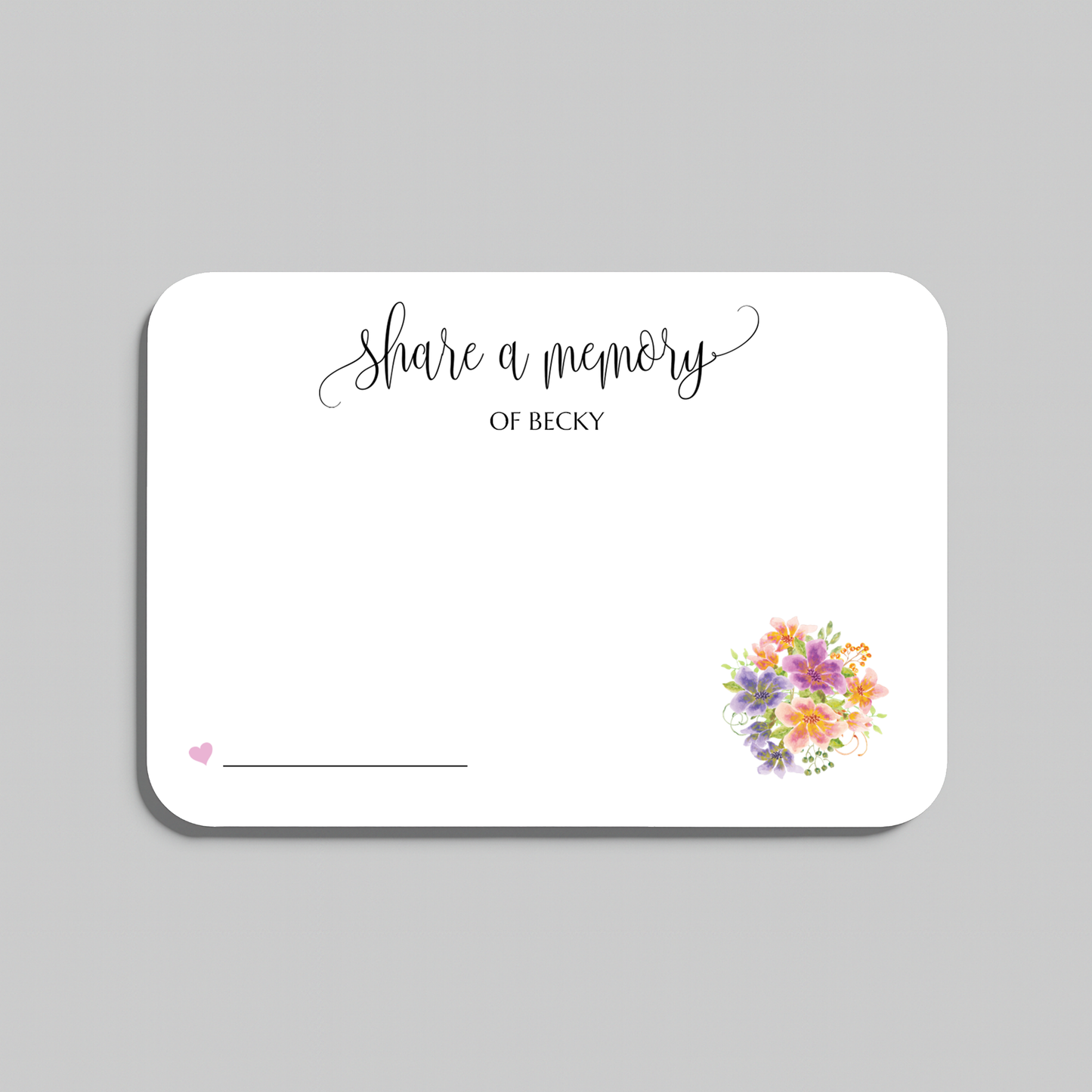 A white rectangular memorial card with rounded corners, printed with the words 'share a memory' in black script and serif text, a small pink heart and line near the lower left, and a small multicolor floral bouquet illustration near the lower right. The card is shown on a light gray background.