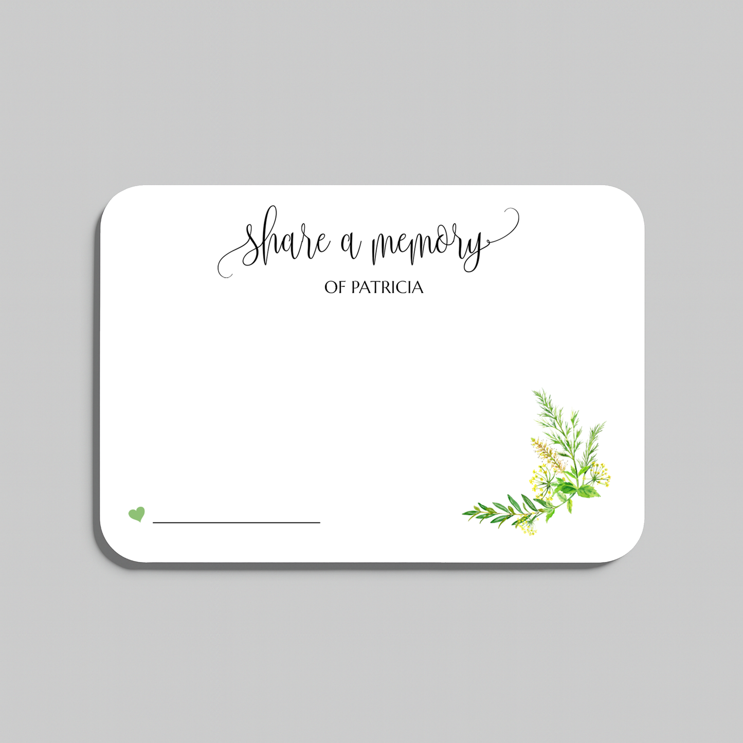 A white rectangular memorial card with rounded corners, featuring the script text 'share a memory' at the top, a small green heart and line at the bottom left, and a delicate green and yellow floral illustration in the lower right corner. The card is centered on a solid gray background.