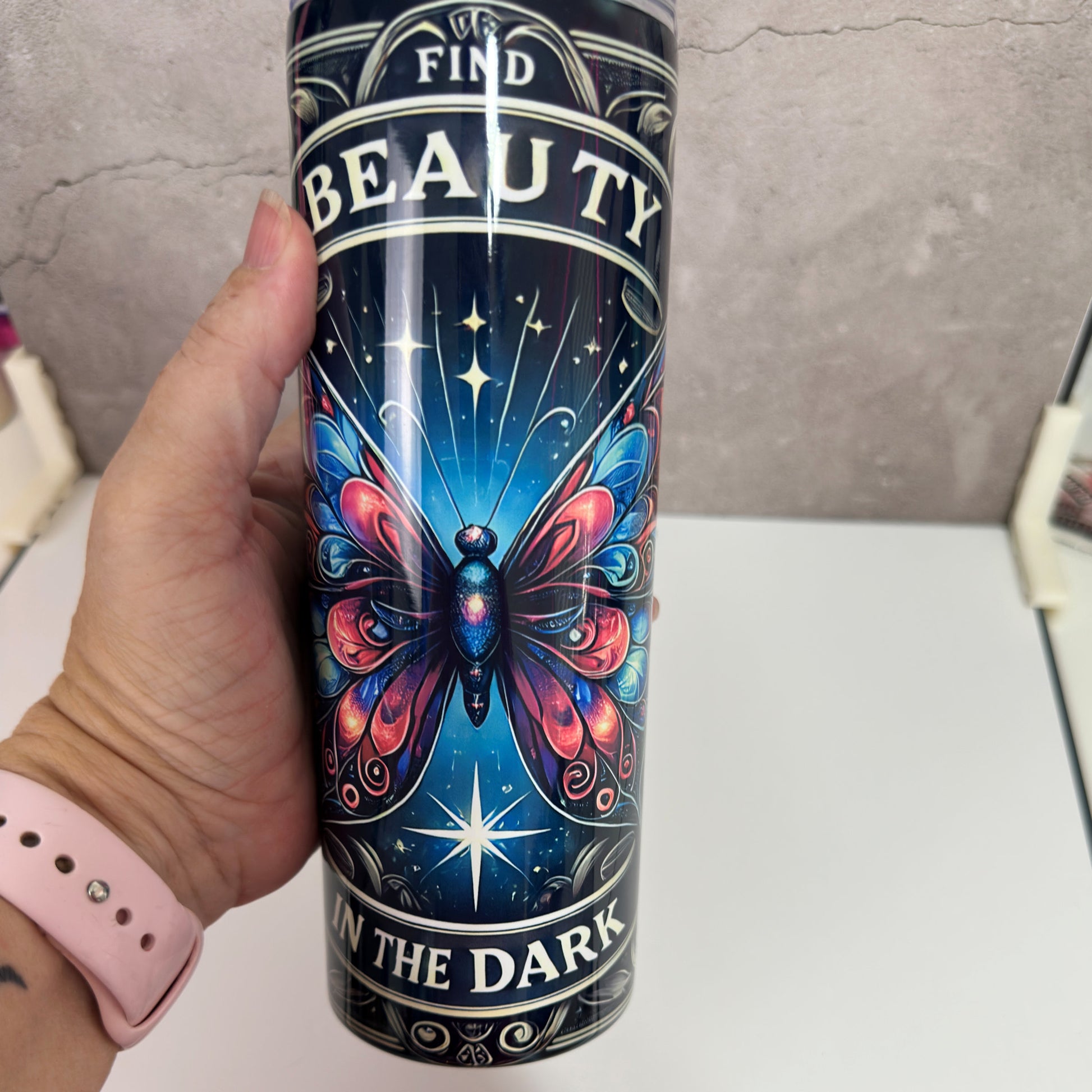 Tumbler with butterfly design and text 'Find Beauty in the Dark' held by a hand.