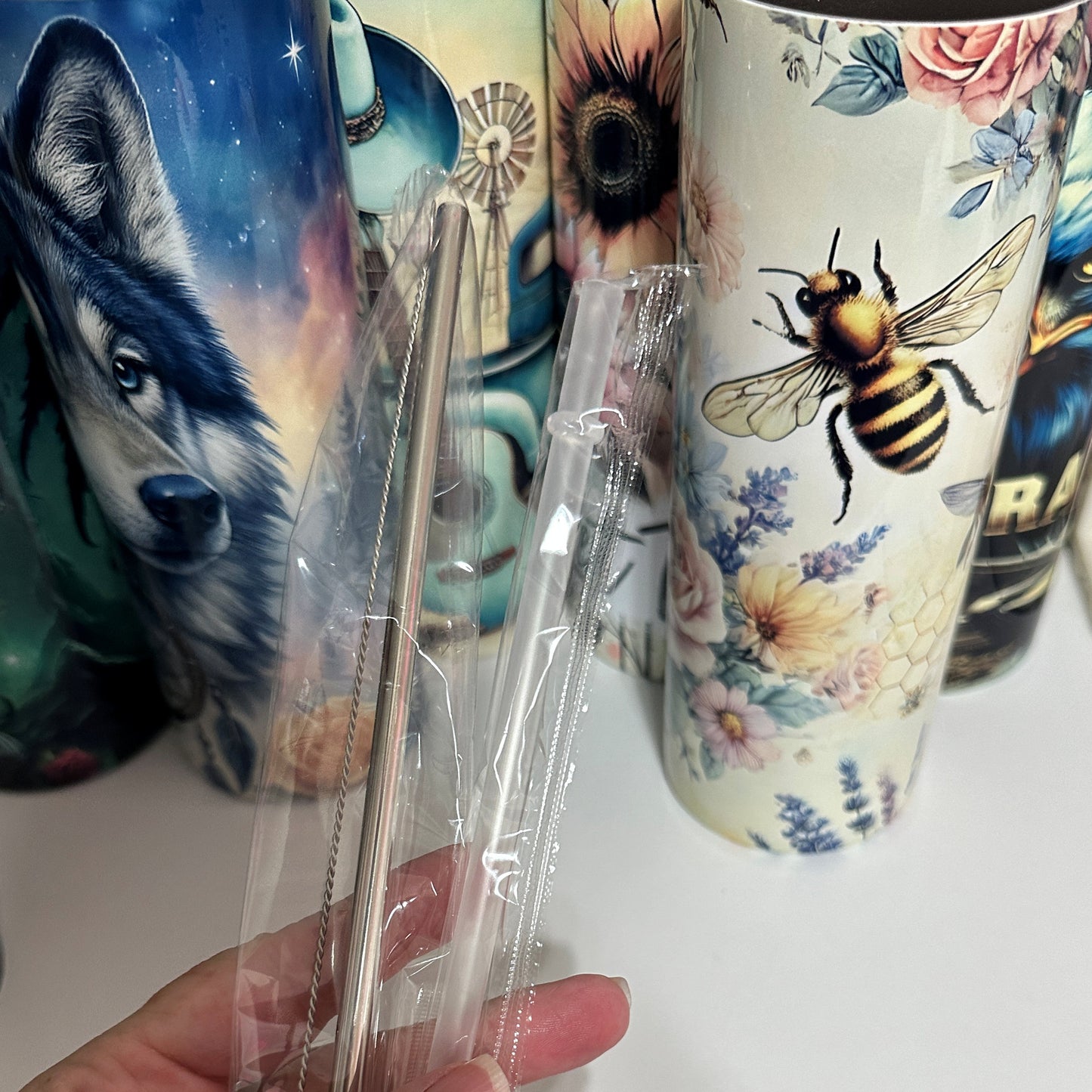 Clear plastic straws held in front of colorful mugs with animal and floral designs.