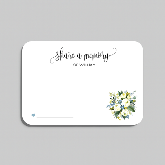 A rectangular white memorial card with rounded corners, featuring the script text 'Share a memory at the top, a small blue heart and line at the bottom left, and a watercolor floral bouquet in white, yellow, and green at the bottom right. The card is shown on a light gray background.