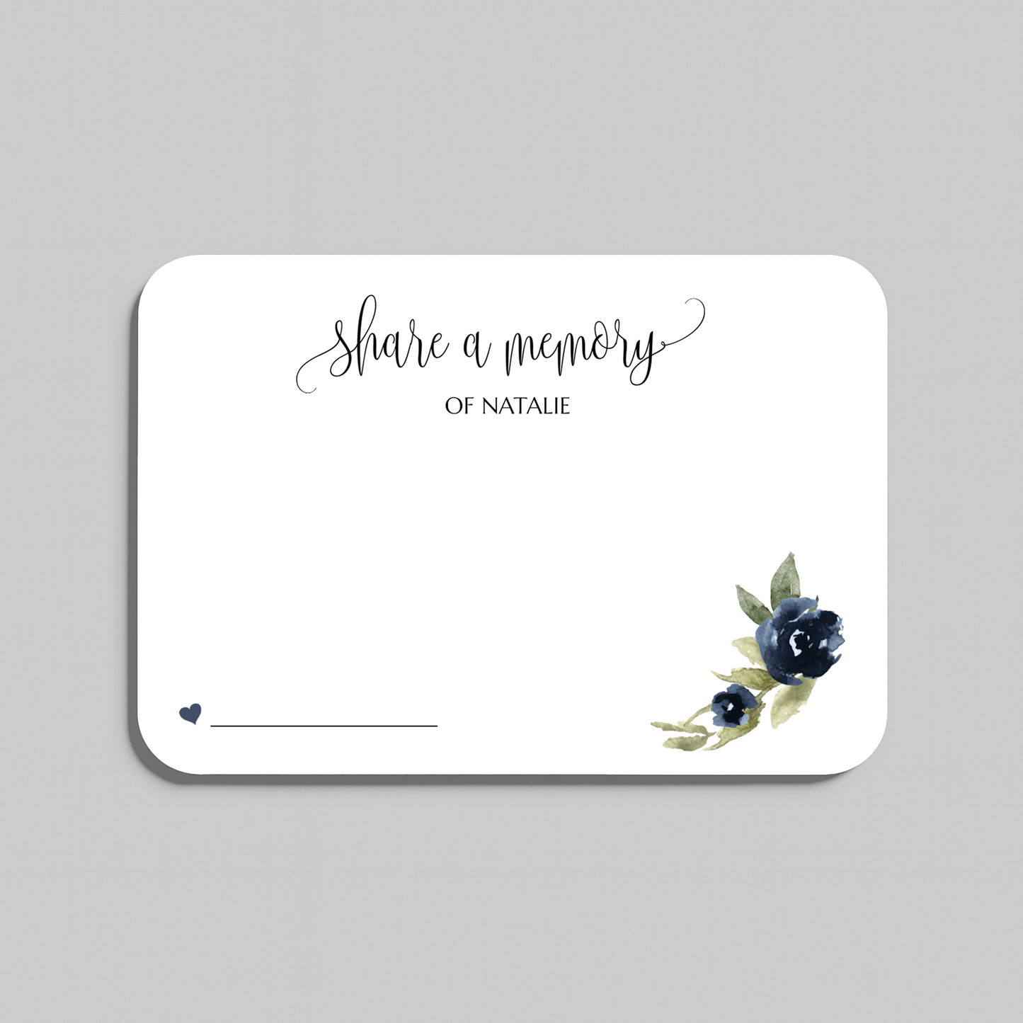 A rectangular white memorial card with rounded corners, featuring the script text 'share a memory  at the top, a small line for writing at the bottom left, and a watercolor floral design in navy blue and green at the bottom right. The card is centered on a light gray background.