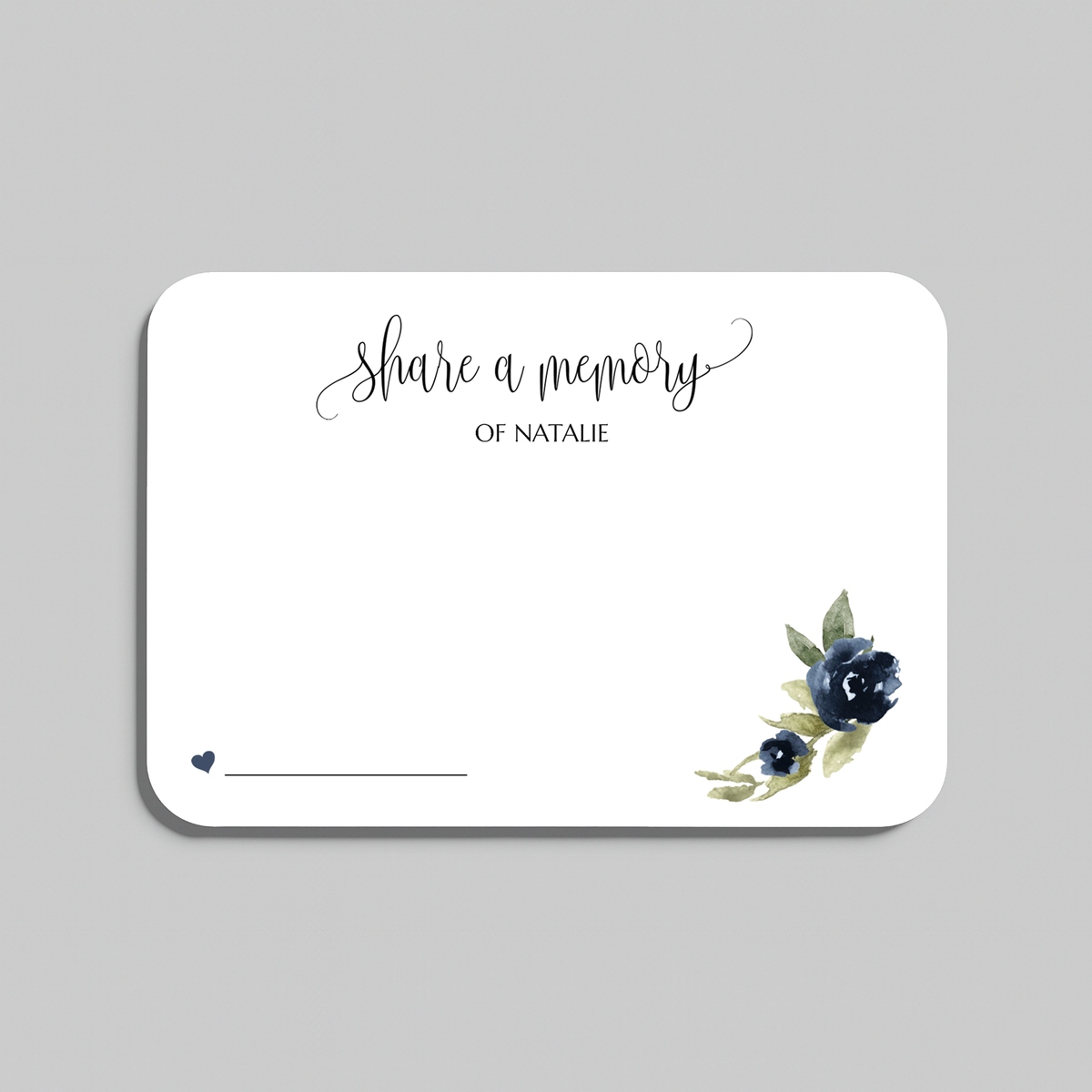 A rectangular white memorial card with rounded corners, featuring the script text 'share a memory  at the top, a small line for writing at the bottom left, and a watercolor floral design in navy blue and green at the bottom right. The card is centered on a light gray background.