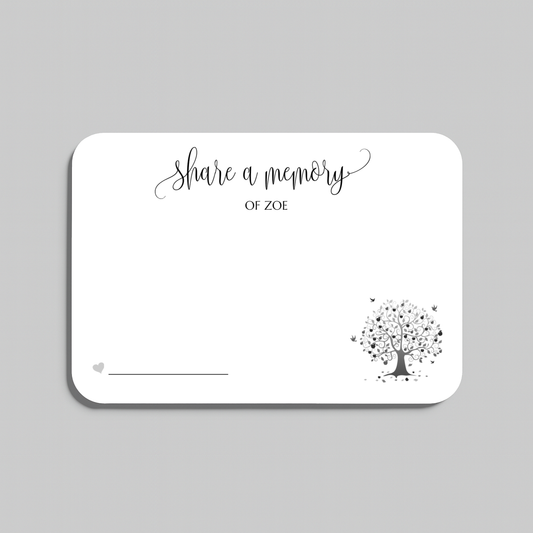 A white rectangular memorial card with rounded corners, featuring the black script text share a memory at the top, a small heart icon with a line at the bottom left, and a black tree illustration with scattered leaves in the lower right. The card is centered on a light gray background.