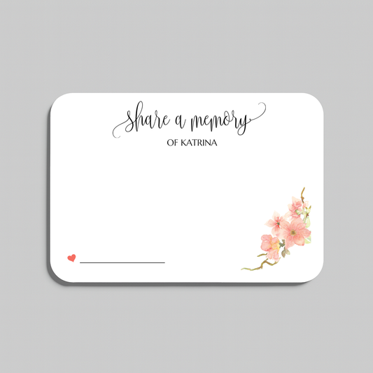 A rectangular white memorial card with rounded corners, printed with the words share a memory in black script and serif text, plus small pink floral artwork in the lower right and a small red heart with a line for writing in the lower left. The card is shown on a light gray background.