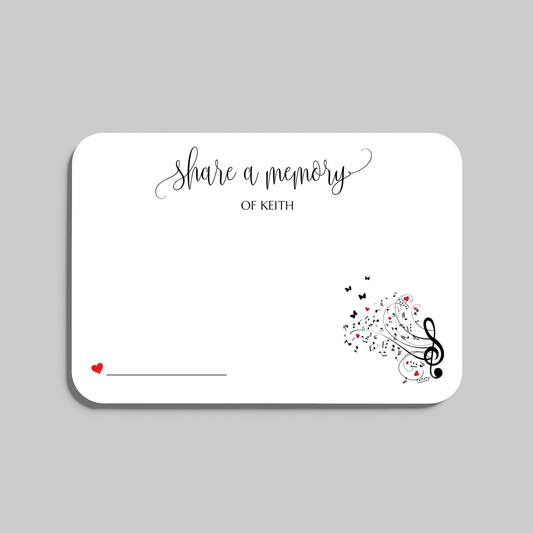A white memorial card with rounded corners, featuring the script text 'share a memory' at the top, a small red heart and line in the lower left, and black musical notes and treble clefs with small red hearts in the lower right. The card is shown on a light gray background.