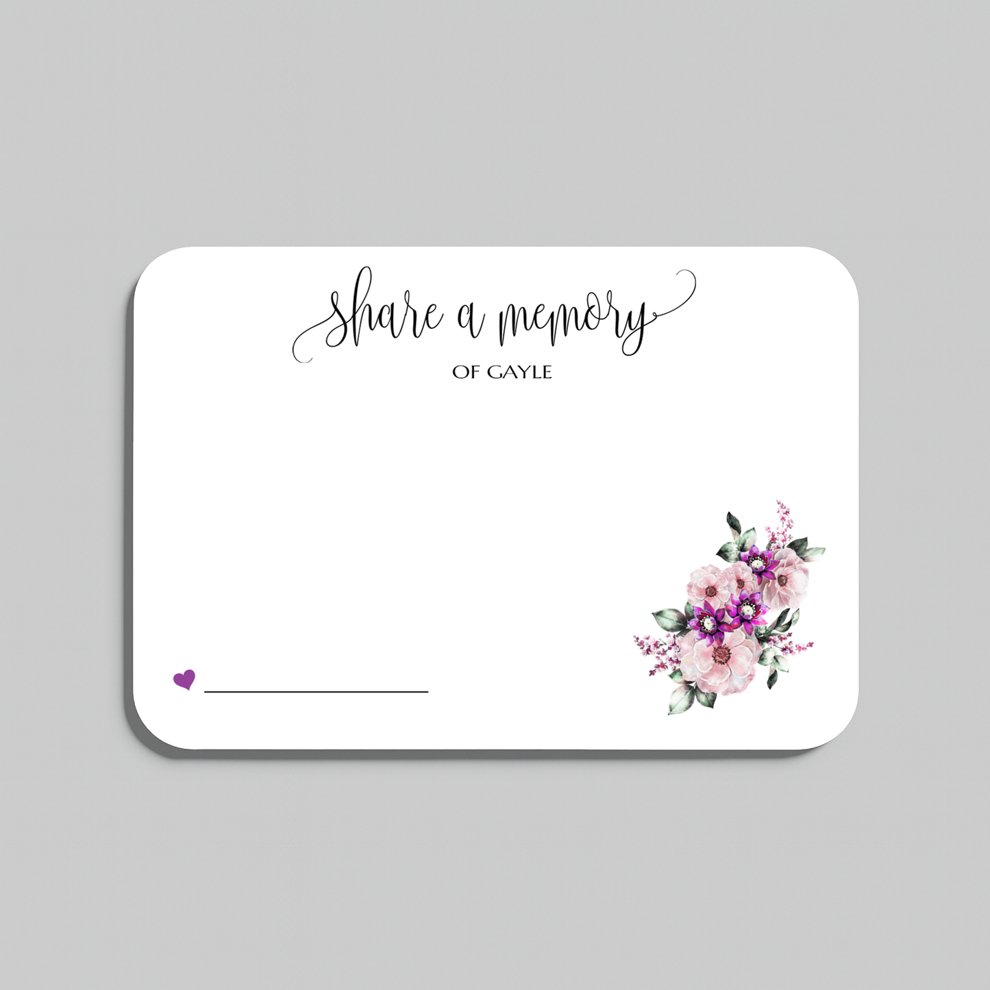 A rectangular white memorial card with rounded corners, featuring the script text 'share a memory' at the top, a small purple heart and line in the lower left, and a watercolor floral bouquet in pink, purple, and green in the lower right. The card is shown on a plain light gray background.