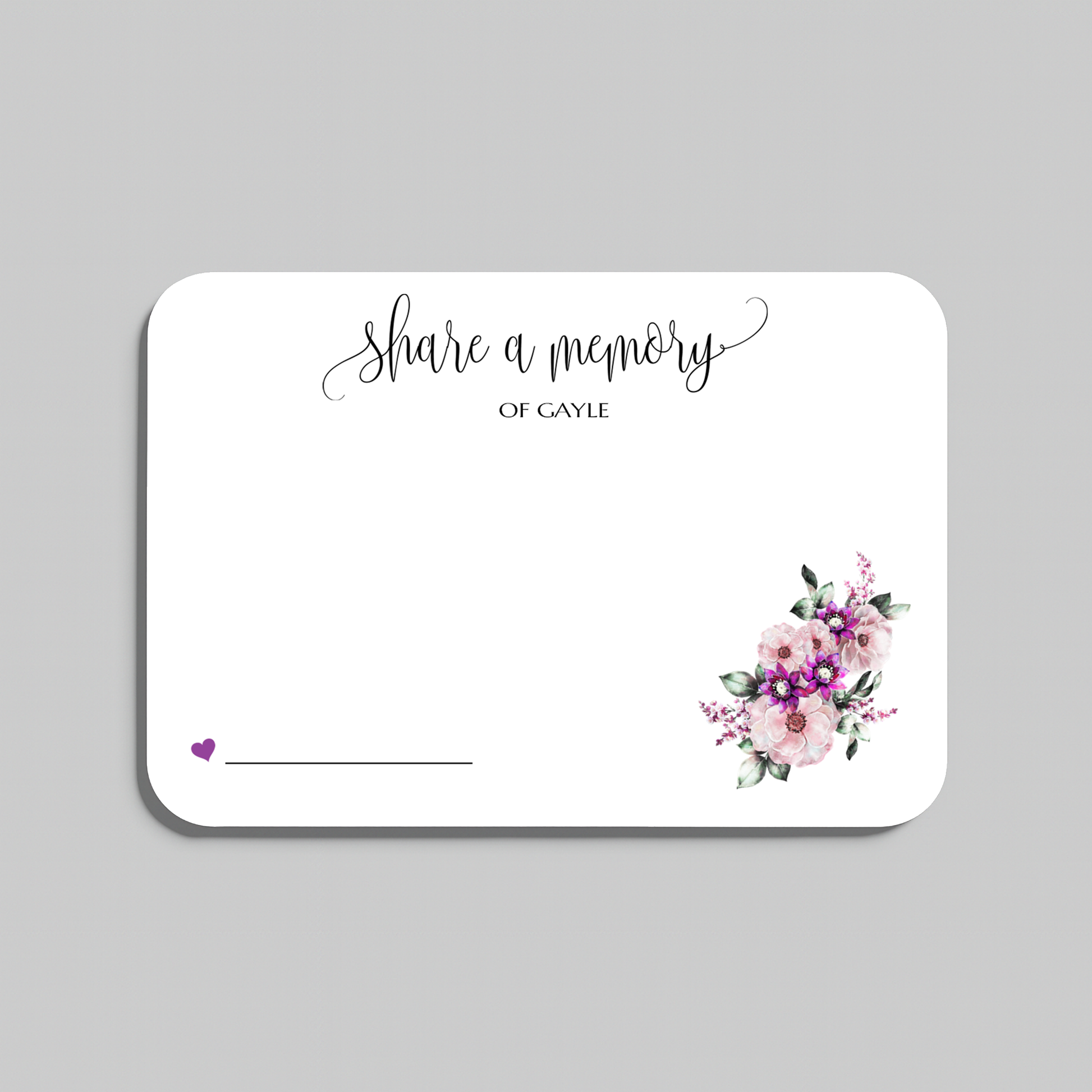 A rectangular white memorial card with rounded corners, featuring the script text 'share a memory' at the top, a small purple heart and line in the lower left, and a watercolor floral bouquet in pink, purple, and green in the lower right. The card is shown on a plain light gray background.