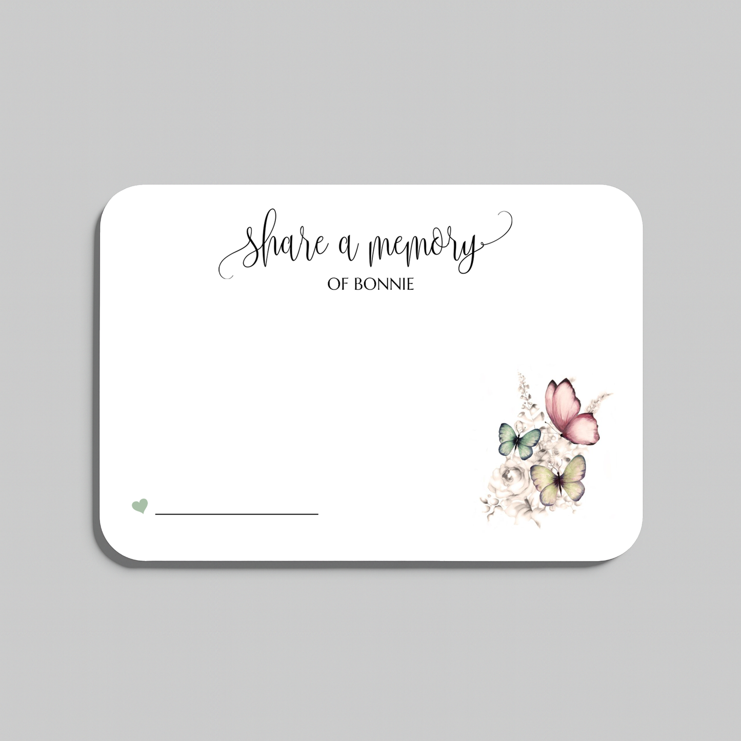A white rectangular memorial card with rounded corners, featuring the script text 'share a memory' and a small floral-and-butterfly illustration in the lower right. The card is shown on a light gray background.