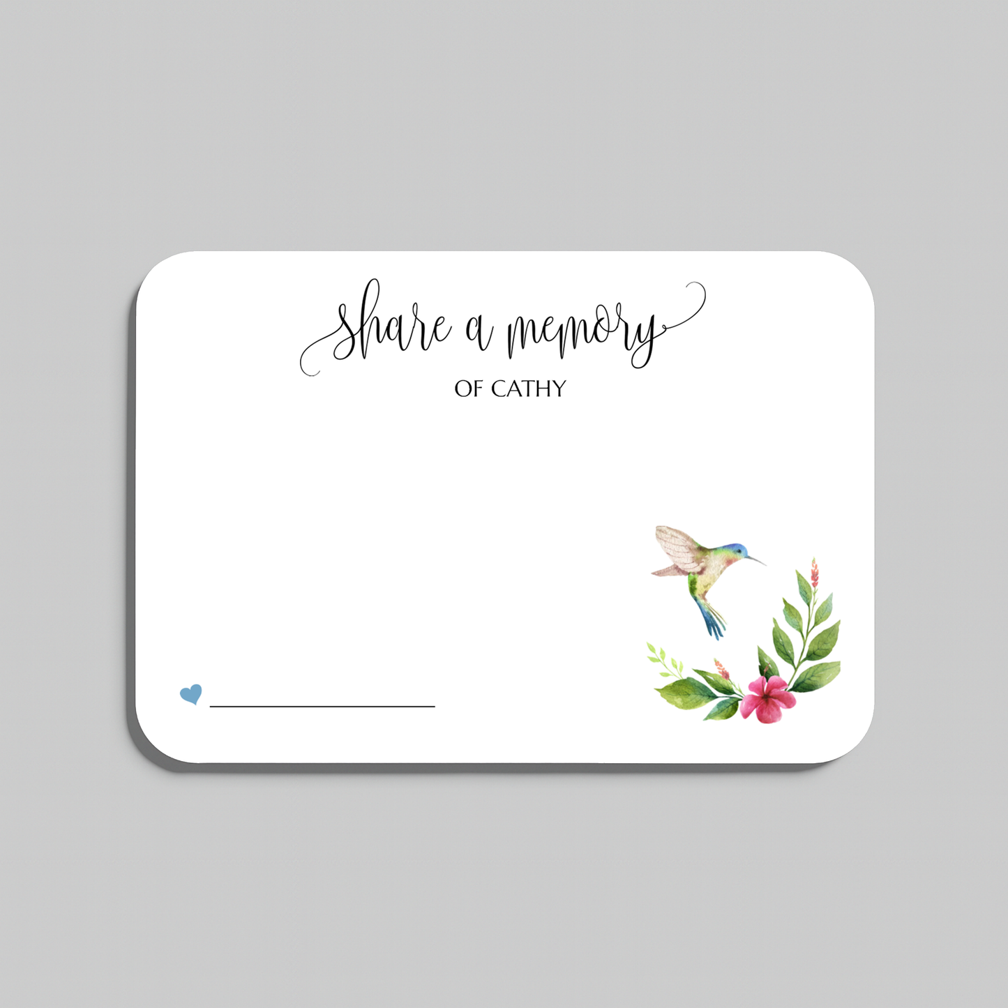 A white memorial guest book card with rounded corners, featuring the script text 'Share a memory' and a watercolor illustration of a hummingbird with green leaves and pink flowers in the lower right corner, shown on a neutral gray background.