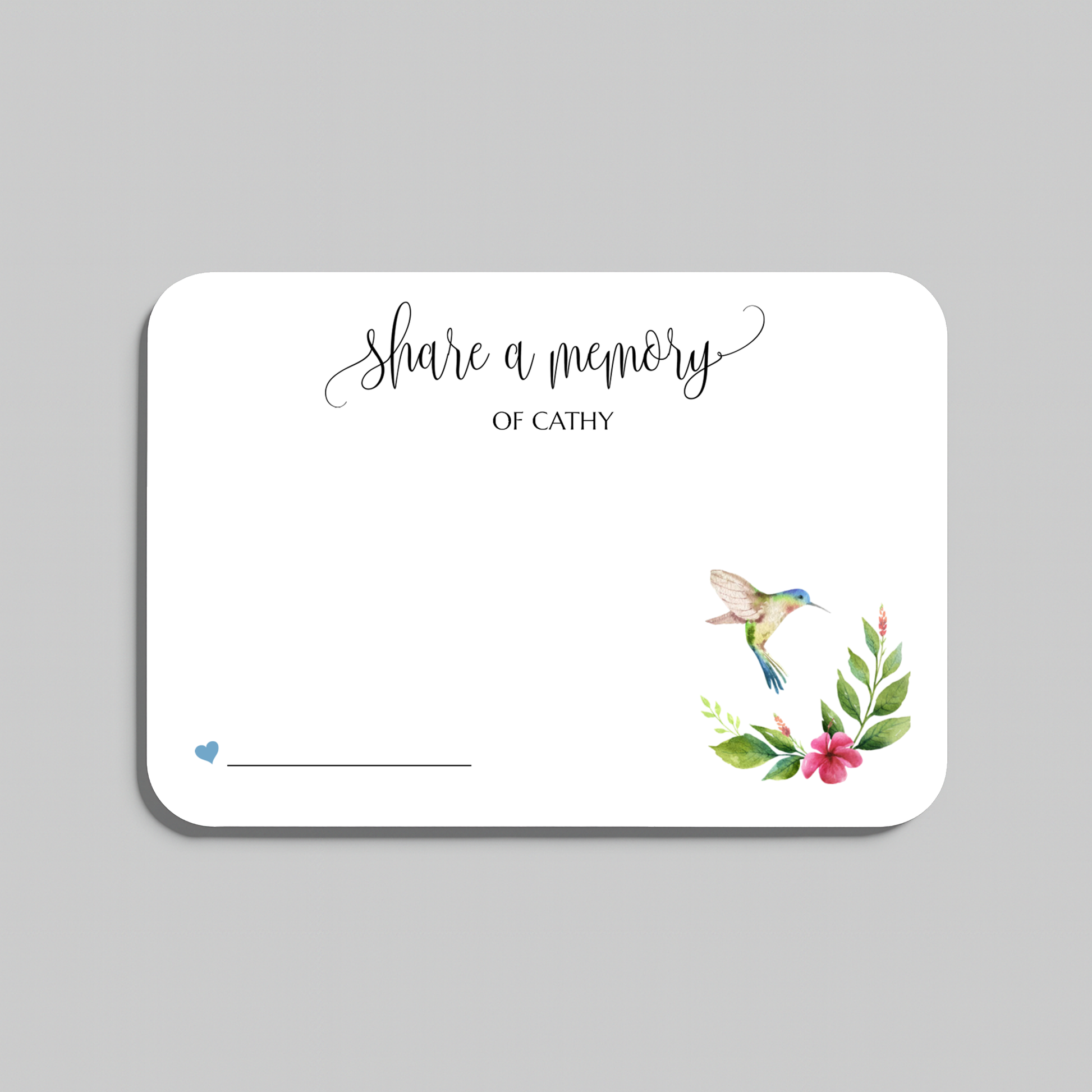 A white memorial guest book card with rounded corners, featuring the script text 'Share a memory' and a watercolor illustration of a hummingbird with green leaves and pink flowers in the lower right corner, shown on a neutral gray background.