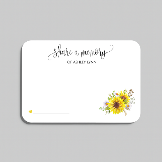 A white memorial keepsake card with rounded corners, featuring the script text 'share a memory' at the top, a small yellow heart and line in the lower left, and a watercolor sunflower and floral arrangement in the lower right. The card is shown on a neutral gray background.