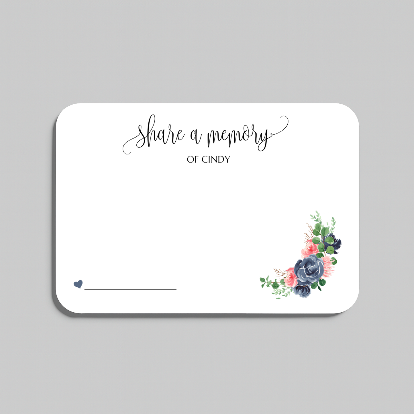 A white rectangular memorial card with rounded corners, featuring the script text 'share a memory' at the top, a blank line at the bottom left, and a small floral arrangement in the lower right corner. The card is shown on a neutral gray background.