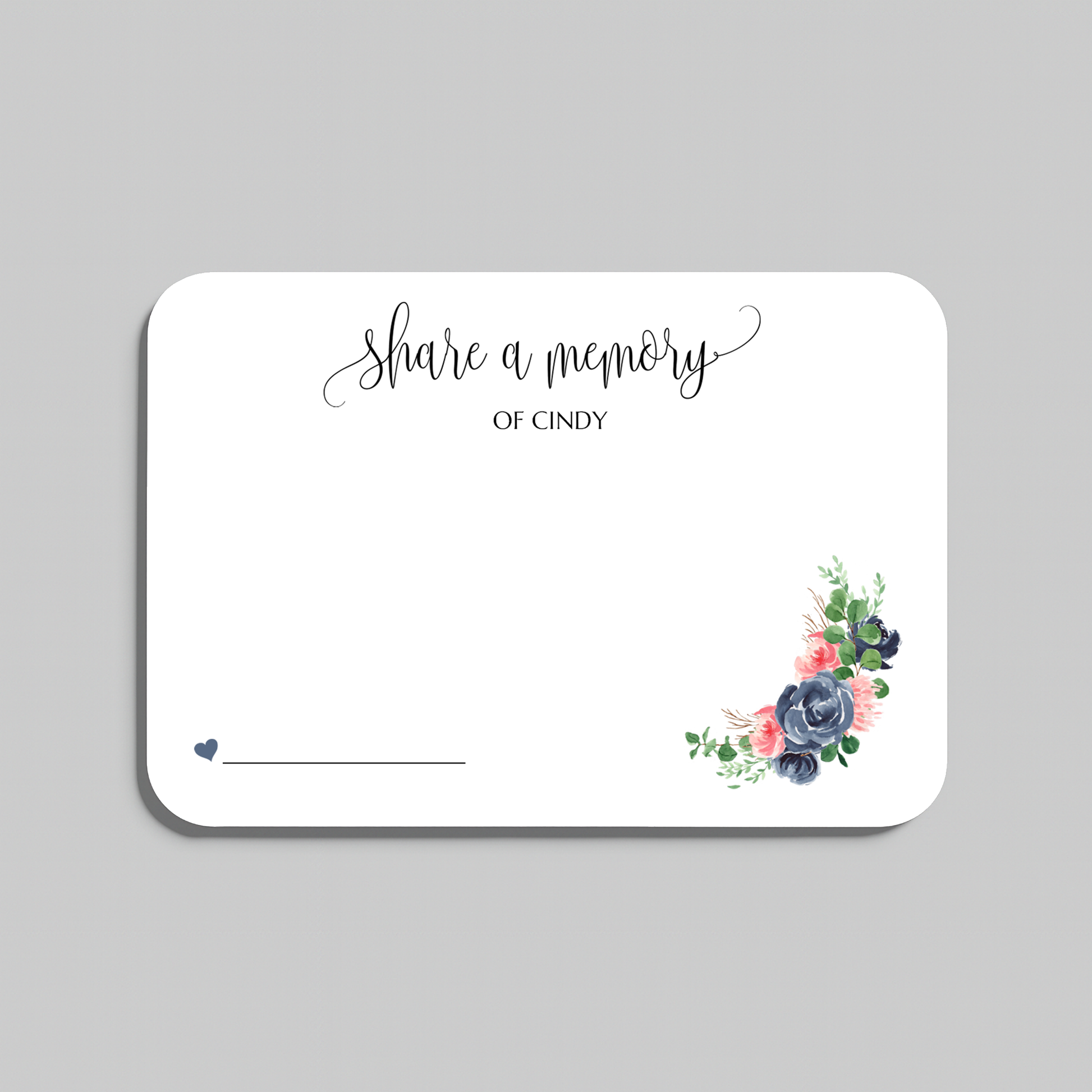 A white rectangular memorial card with rounded corners, featuring the script text 'share a memory' at the top, a blank line at the bottom left, and a small floral arrangement in the lower right corner. The card is shown on a neutral gray background.