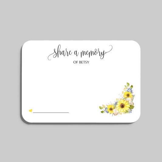 A white rectangular memorial card with rounded corners, featuring the script text 'share a memory' at the top, a blank line at the bottom left for writing a name, and a watercolor sunflower cluster in yellow, green, and blue at the bottom right. The card is shown on a neutral gray background.