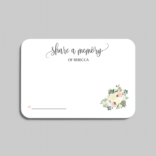 A rectangular white memorial card with rounded corners, printed with the words 'share a memory' in black script and serif text, plus a small floral bouquet illustration in soft pink, cream, and green near the lower right. The card is shown on a light gray background.