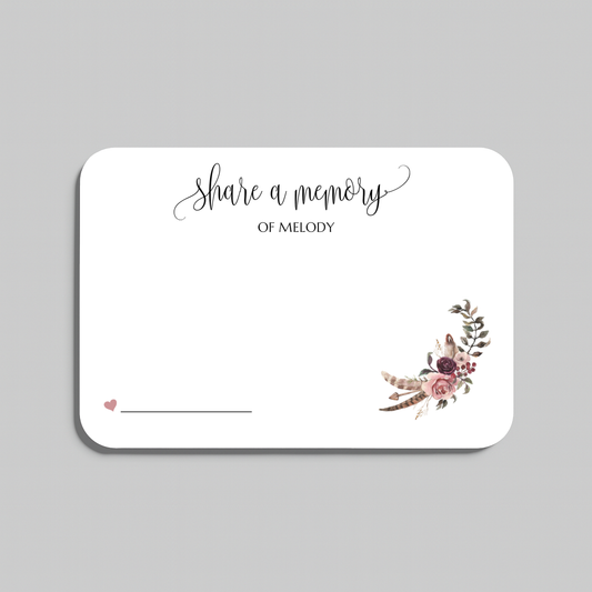 A rectangular white wedding reception card with rounded corners, featuring the script text 'share a memory' at the top, a small pink heart and writing line in the lower left, and a boho floral bouquet illustration in the lower right. The card is shown on a neutral gray background.