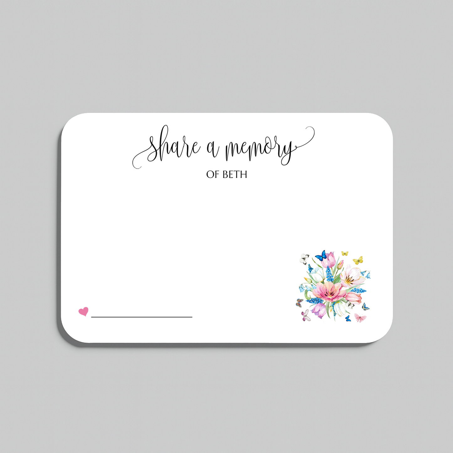 A white rectangular memorial card with rounded corners, featuring the script text 'share a memory' at the top, a small pink heart and line in the lower left, and a colorful floral bouquet illustration in the lower right. The card is shown on a light gray background.