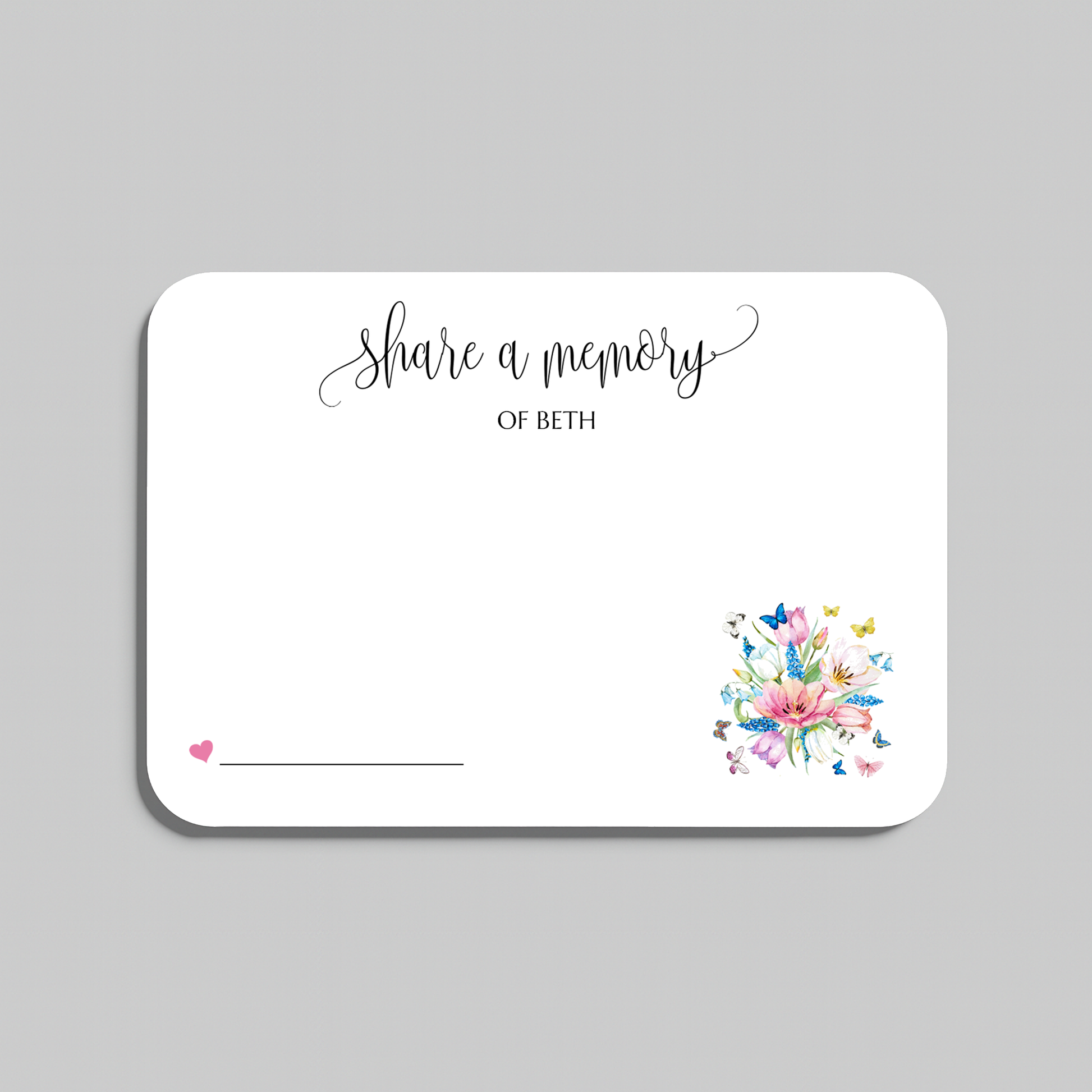 A white rectangular memorial card with rounded corners, featuring the script text 'share a memory' at the top, a small pink heart and line in the lower left, and a colorful floral bouquet illustration in the lower right. The card is shown on a light gray background.
