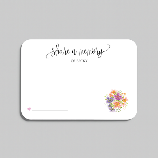 A white rectangular memorial card with rounded corners, printed with the words 'share a memory' in black script and serif text, a small pink heart and line near the lower left, and a small multicolor floral bouquet illustration near the lower right. The card is shown on a light gray background.