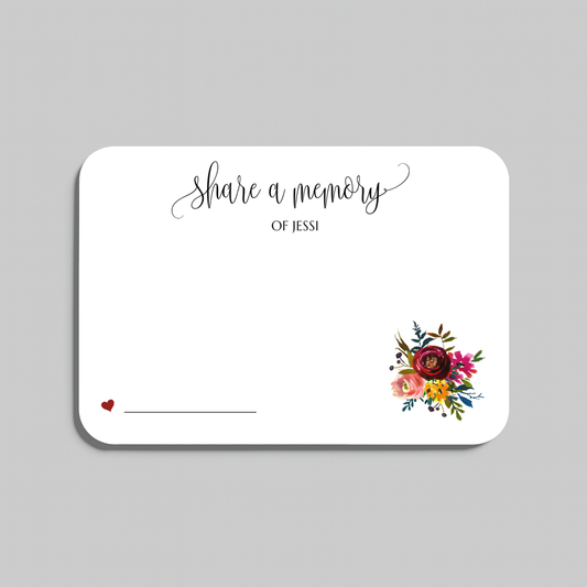 A white rectangular memorial card with rounded corners, printed with the words 'share a memory' in black script and serif text, a small red heart and line on the lower left, and a colorful floral bouquet illustration on the lower right. The card is centered on a light gray background.