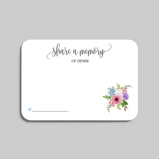 A white rectangular memorial card with rounded corners, featuring the script text 'share a memory' at the top, a blank line at the bottom left, and a small watercolor floral arrangement in the lower right corner. The card is shown on a neutral gray background.