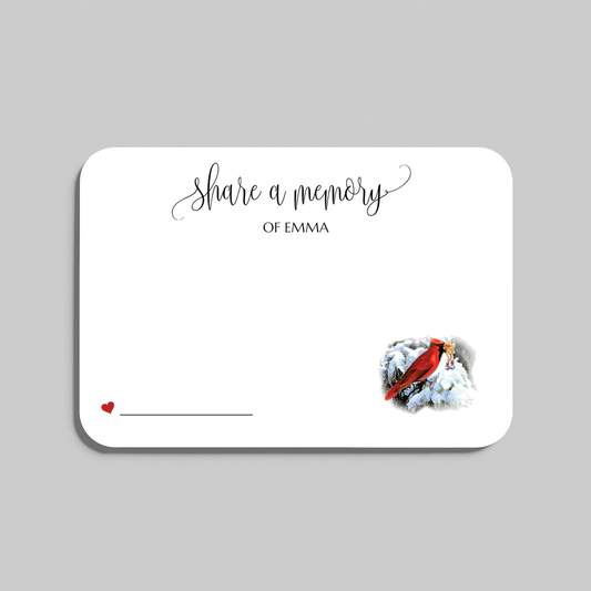 A memorial card with rounded corners on a light gray background. The card is white with black script text reading 'share a memory' a small red heart and line in the lower left, and a small red cardinal perched on white snow in the lower right.