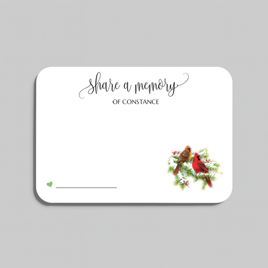 A rectangular white memorial card with rounded corners, featuring the script text 'share a memory' at the top and a small illustration of two cardinals on a branch in the lower right corner. The card is shown on a plain light gray background.