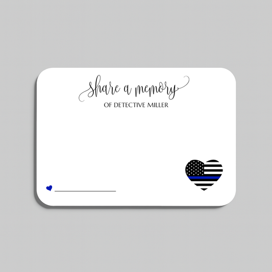 A white rectangular memorial card with rounded corners on a light gray background. The card features the script text 'share a memory' at the top, a small blue heart and line on the lower left, and a black-and-white striped heart with a blue stripe on the lower right for law enforcement memorials