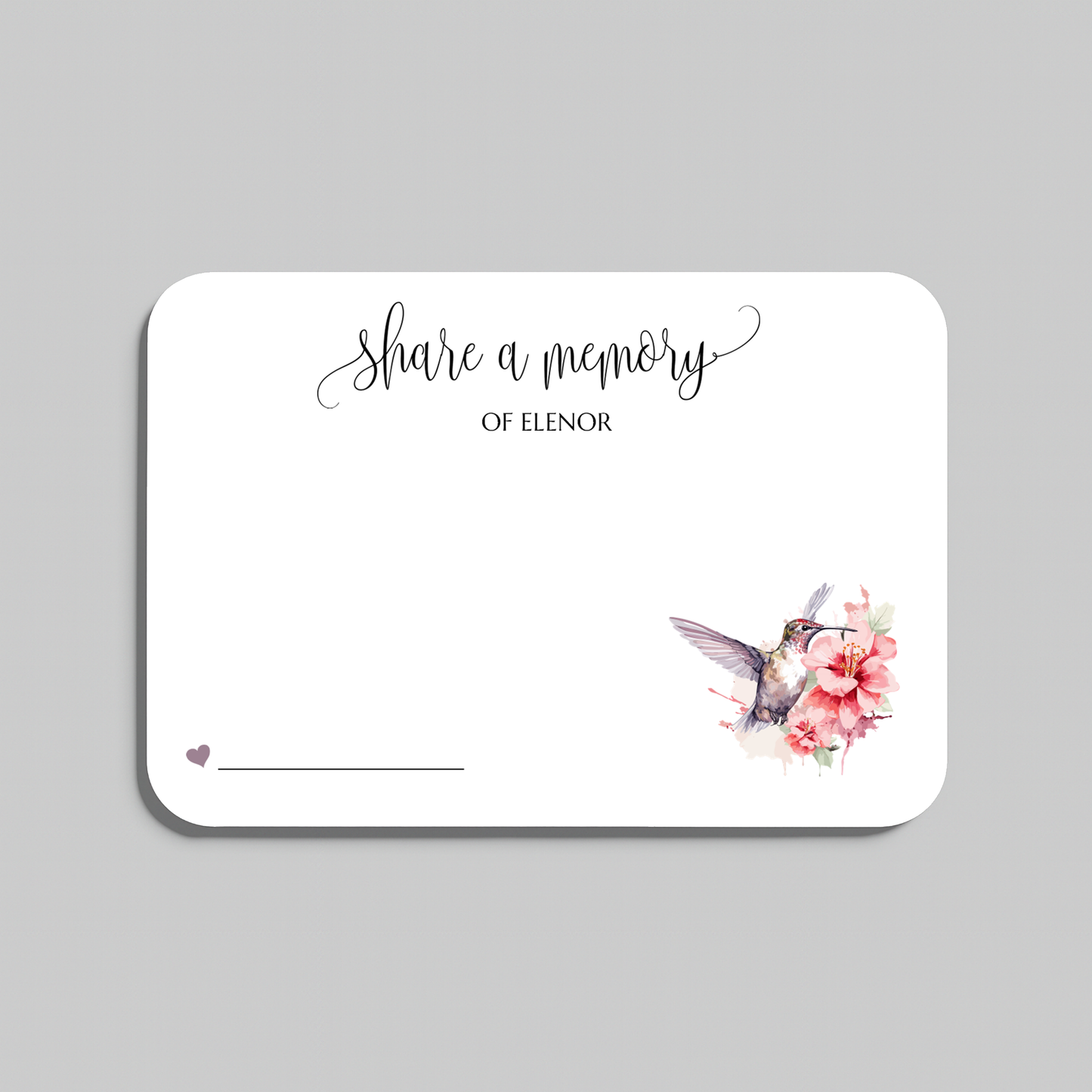 A rectangular white memorial card with rounded corners, featuring the script text 'share a memory' at the top, a small heart and line in the lower left, and a watercolor hummingbird with pink flowers in the lower right. The card is shown on a light gray background.